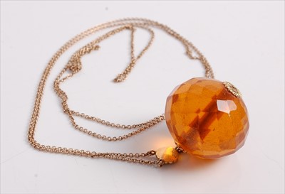 Lot 475 - A faceted clear orange amber ball pendant, of...