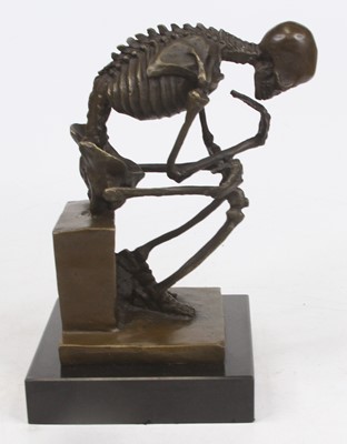 Lot 621 - A bronzed model of a skeleton, shown in seated...