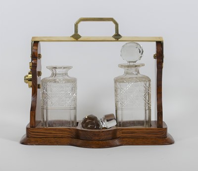 Lot 51 - An oak and brass two-decanter tantalus, having...