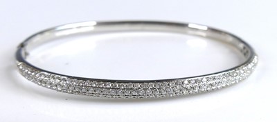 Lot 2328 - An 18ct white gold diamond hinged oval bangle,...