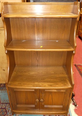 Lot 1233 - An Ercol mid-elm bow front waterfall bookshelf,...