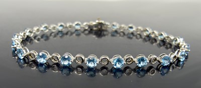Lot 2582 - A 9ct white gold blue topaz line bracelet, set...